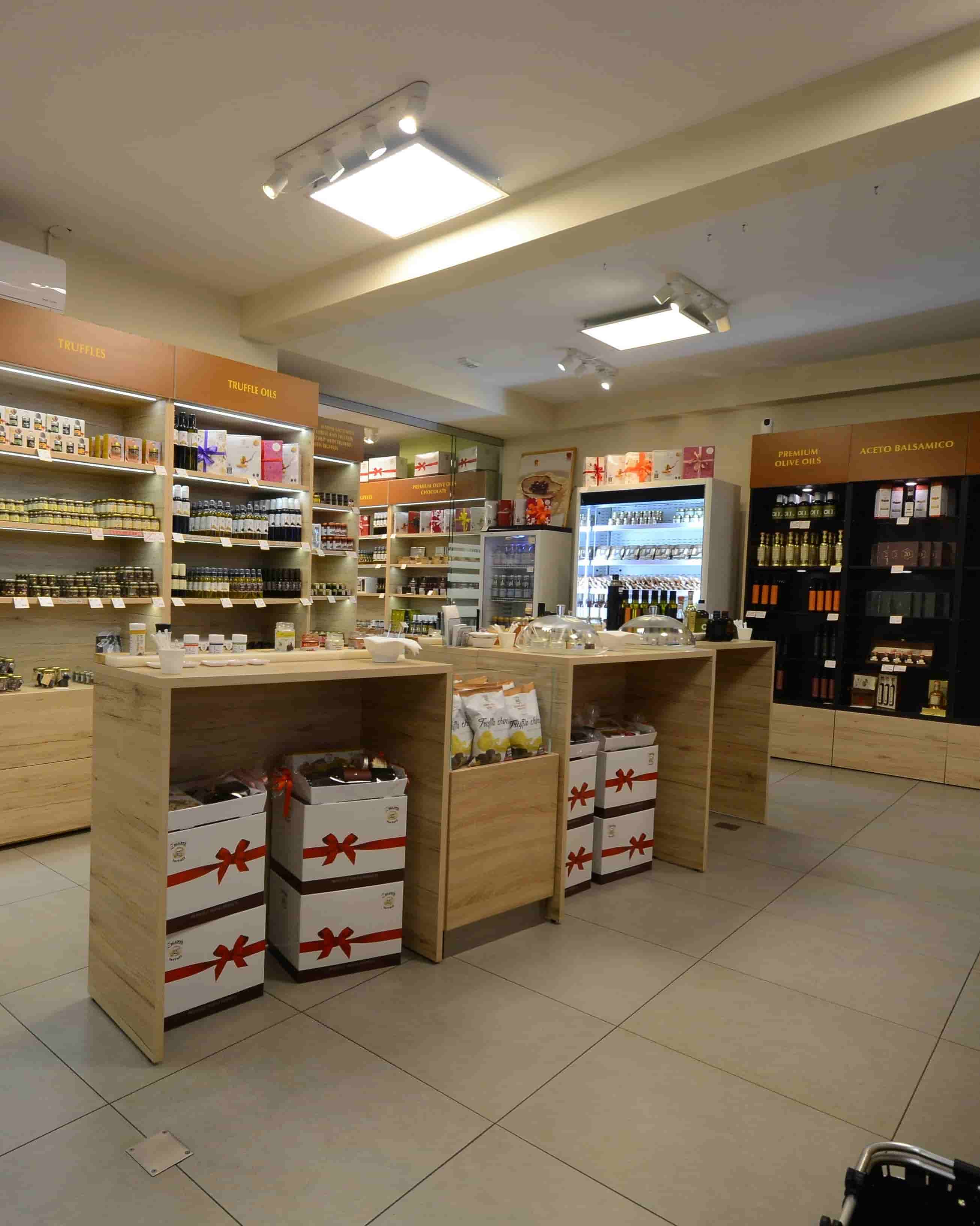 A retail store interior with wooden display counters, shelves stocked with packaged goods, a refrigerated display case, and tiled flooring under ceiling track lighting.